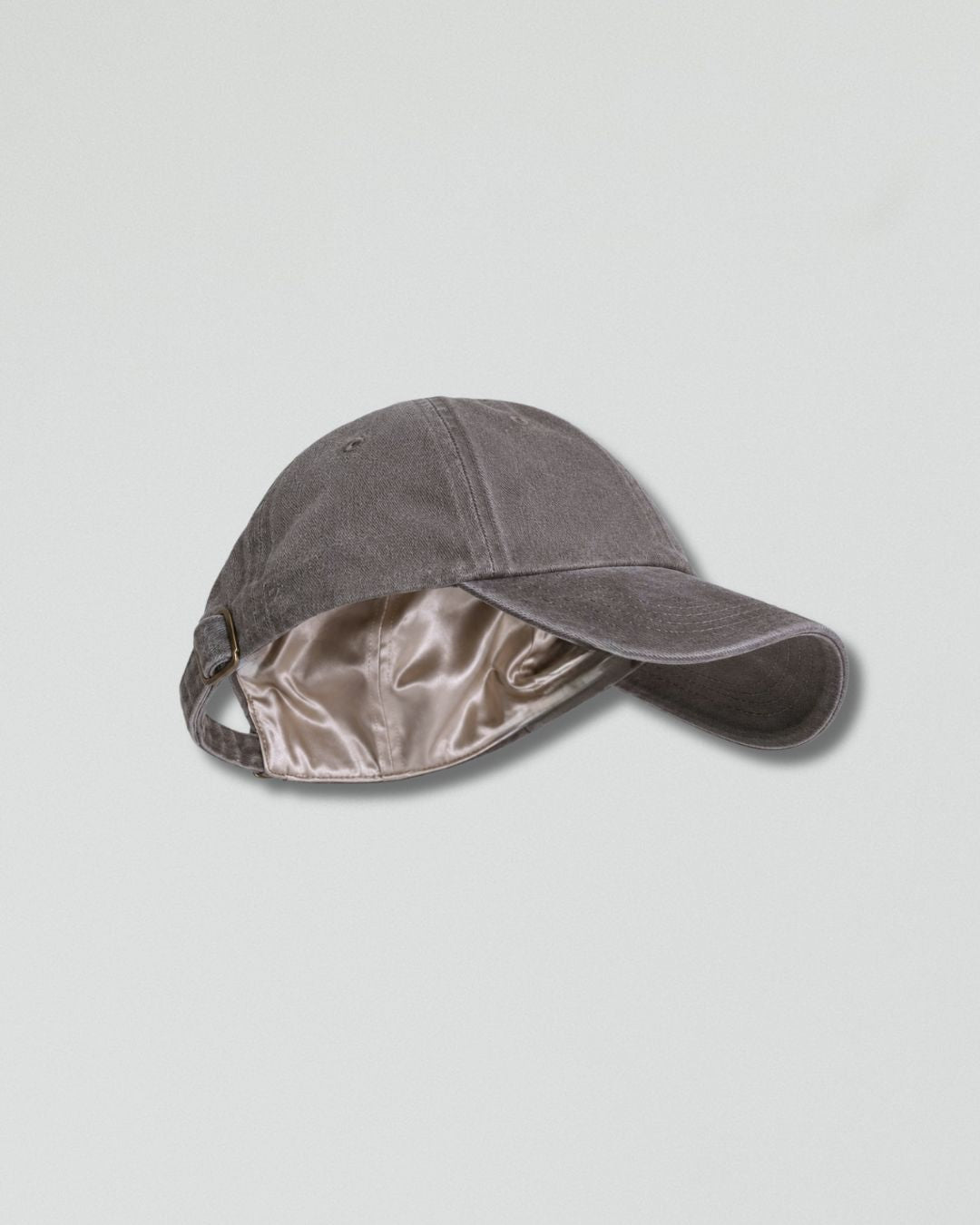 A dark gray baseball cap with a shiny taupe satin lining, shown from a side angle on a light gray background.