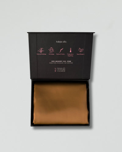 Brown silk pillowcase in an open black box with brand details on a light gray background