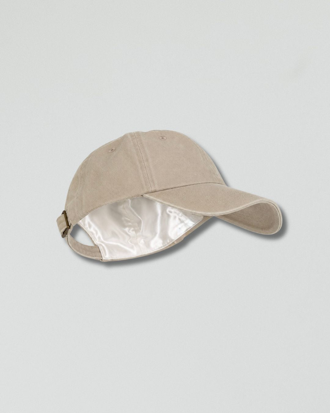 A light beige baseball cap with a shiny silver interior lining, shown from a side angle on a light gray background.