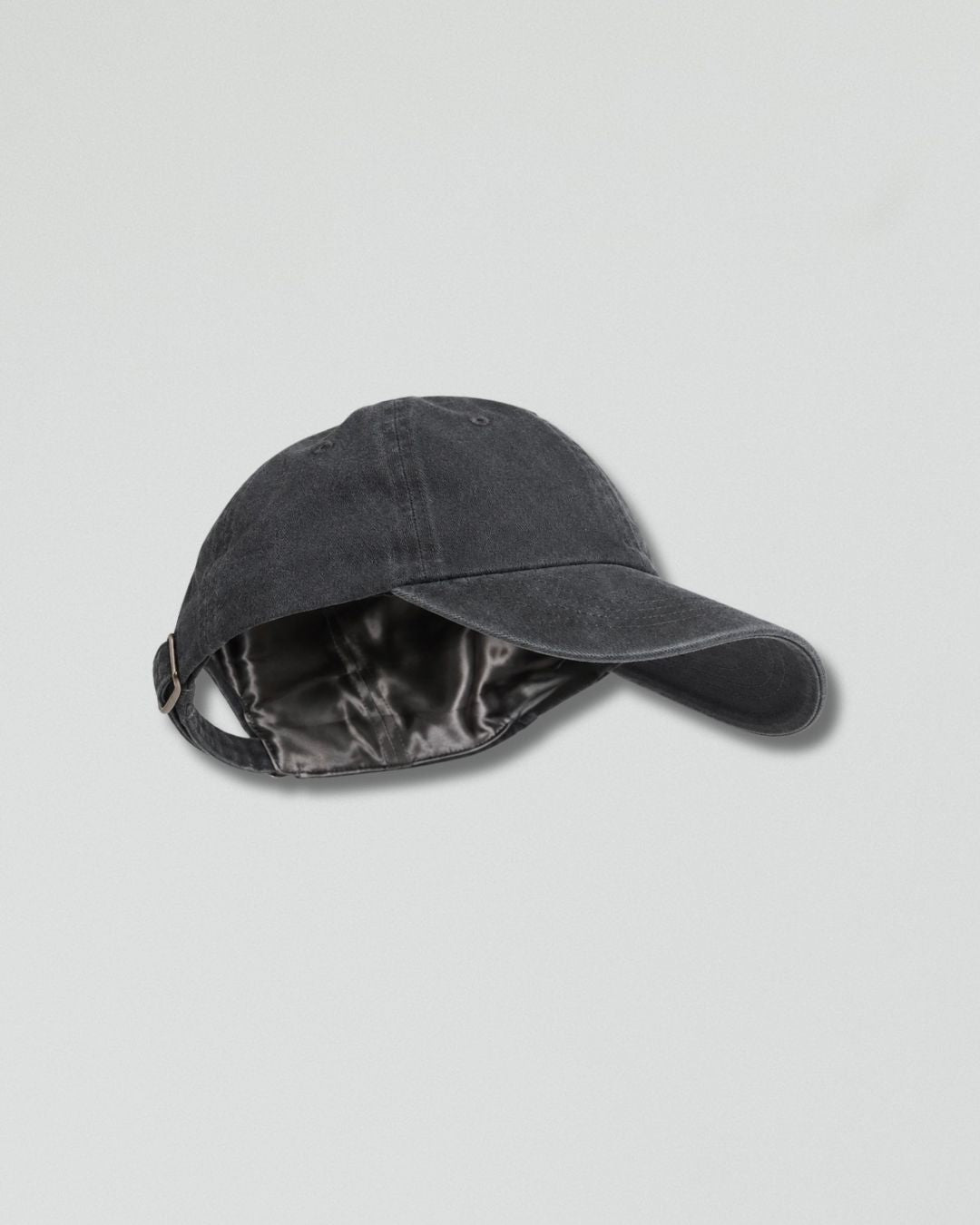 A dark gray washed cotton baseball cap with a satin black inner lining, shown from a side angle on a light gray background.