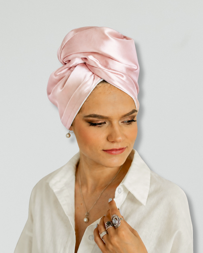 A woman wearing a light pink siilk turban headwrap and a white collared shirt, photographed against a plain light gray background.